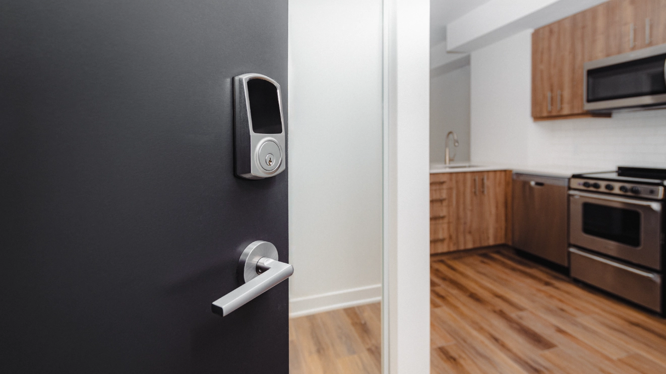 A wireless smart lock installed on an apartment door, with the unit’s kitchen visible through the open doorway