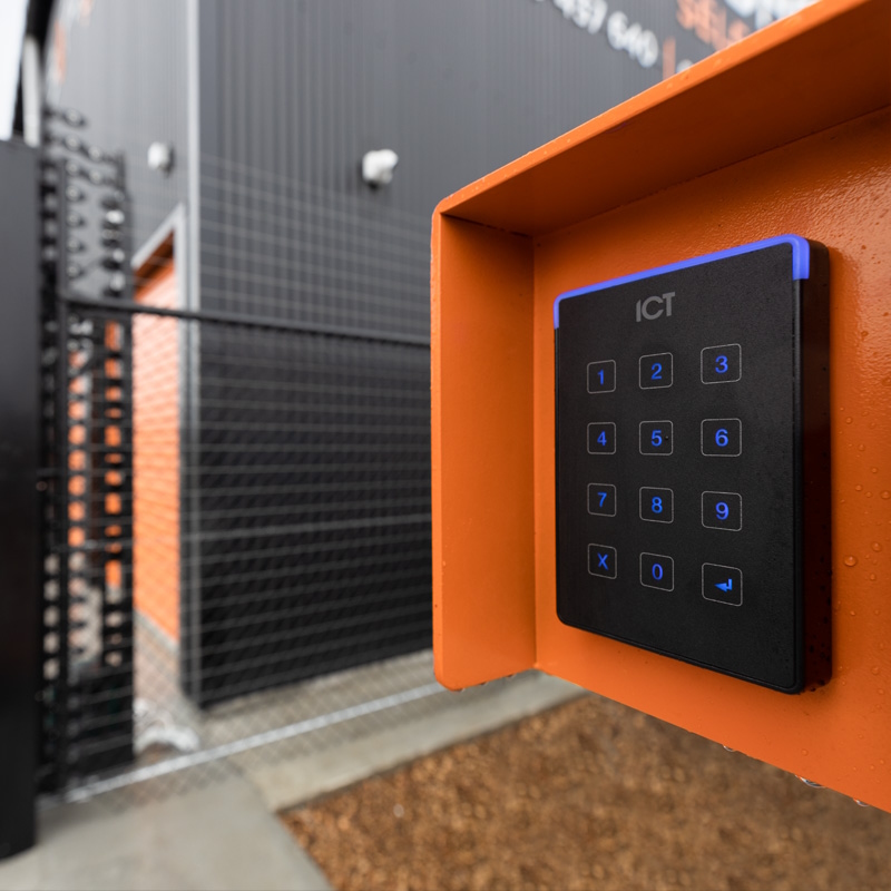 Black access control keypad reader in an orange metal mount