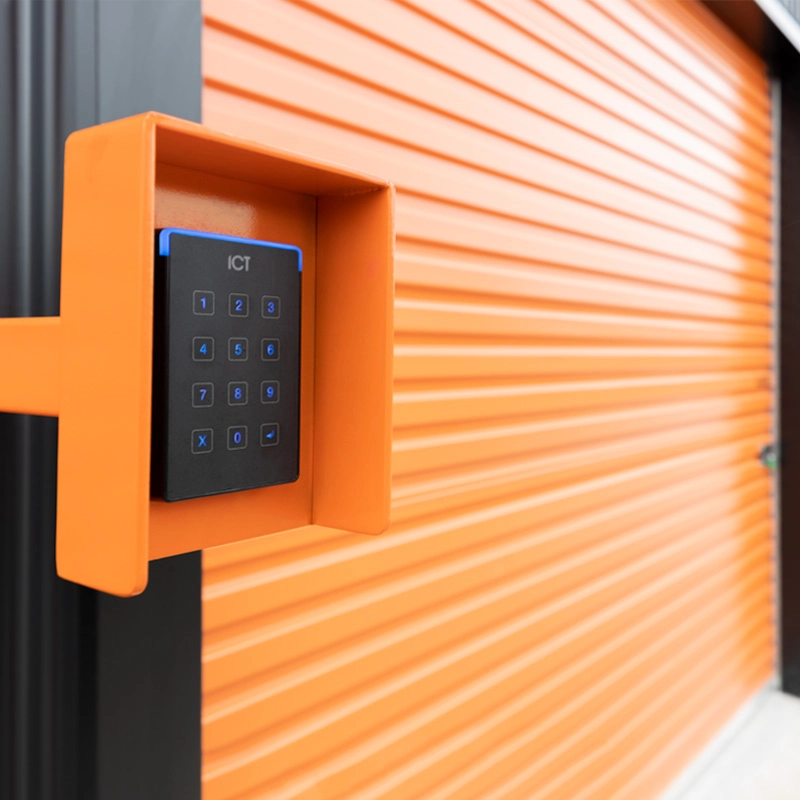 Black ICT keypad access control reader on an orange mount with orange roller door in the background