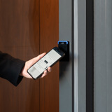A hand holding a smartphone touching it to an access control reader for entry into a building